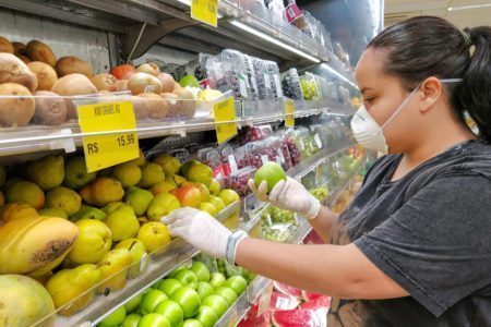 Latina picking out food fruit at grocery store wearing mask for covid coronavirus