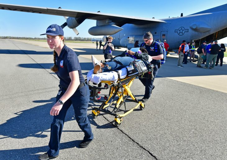 Two medical emergency specialists push patient on gurney at airport during exercise.