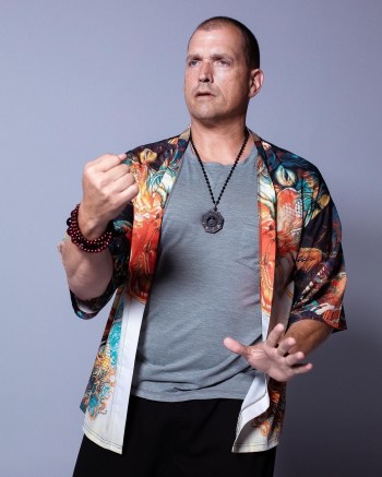 Tai Chi instructor in a colorful jacket and gray shirt holds a martial arts pose.